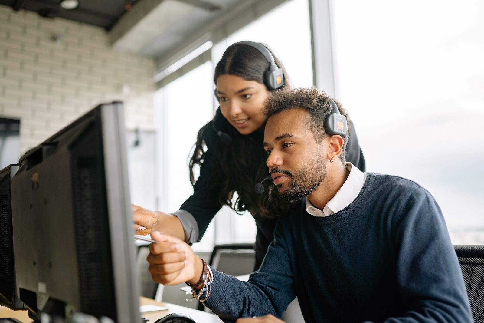 Claims consultant in a headset pointing at a colleague's screen in a modern contact centre